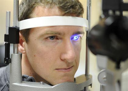 An Eye care professional conducting an eye exam with a man wearing a blue light on his head.