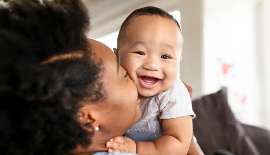 A woman is holding a baby and smiling, conveying a heartwarming scene of maternal joy.