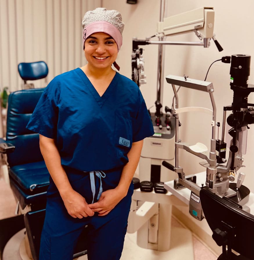 A woman in scrubs, an optometrist, standing in front of an eye machine, delivering expert eye care to address vision loss.