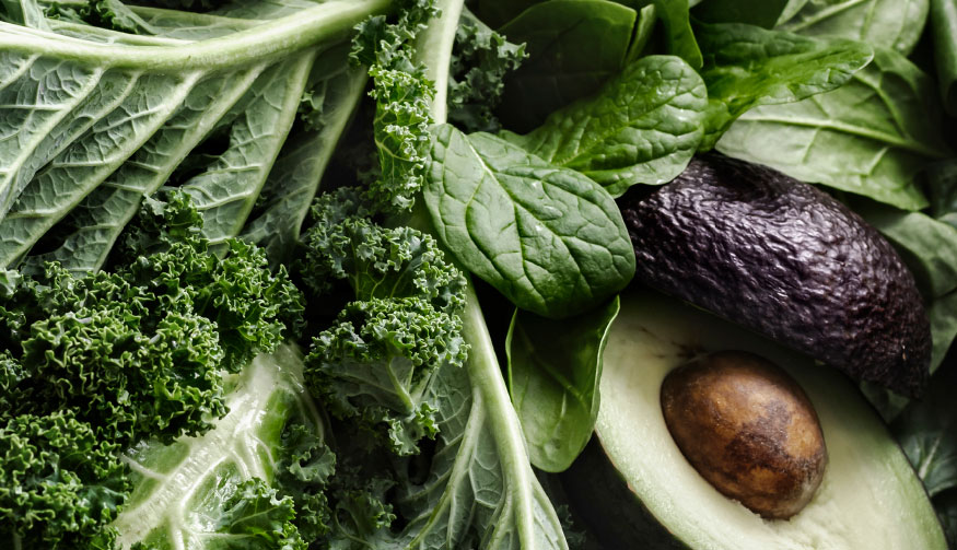 A variety of nutritious vegetables, including kale and avocado, are meticulously arranged on a table.