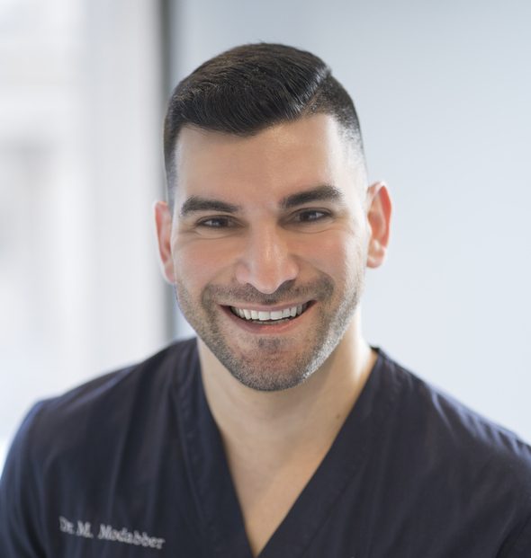 A smiling man in a blue scrub shirt who is an optometrist.