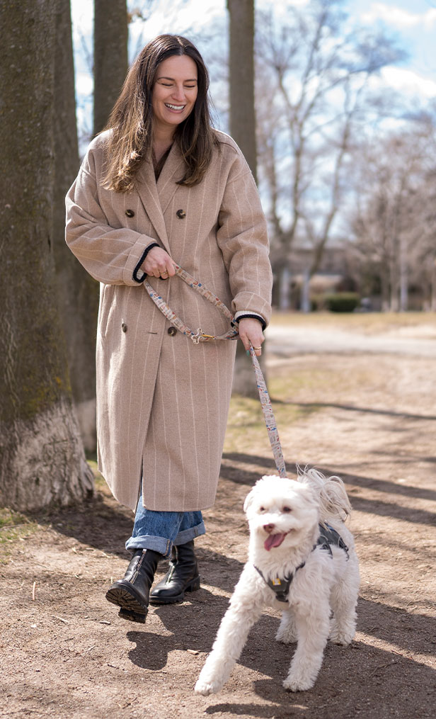 A woman walking her dog in a beige coat.