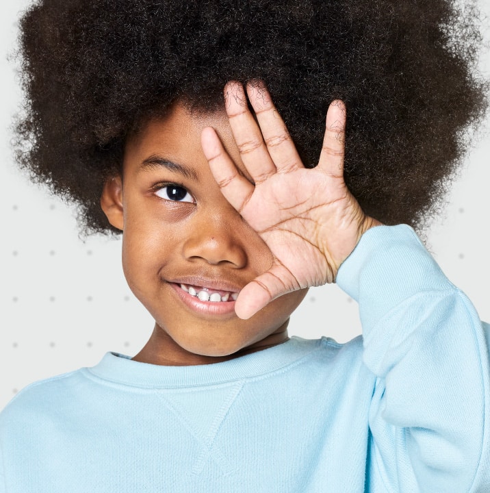 A young girl with afro hair making a sign with her hands while receiving eye care.