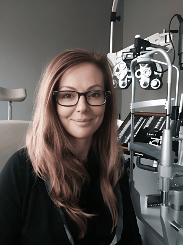 A woman in glasses is sitting in front of an eye machine at an eye doctor's office, ensuring her eye health and screening for potential eye diseases.