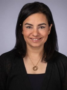 A smiling woman wearing a black shirt and necklace, promoting eye health.