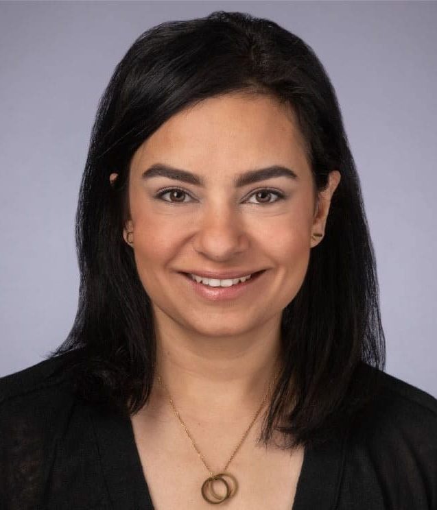 A smiling woman wearing a black shirt and necklace, promoting eye health.