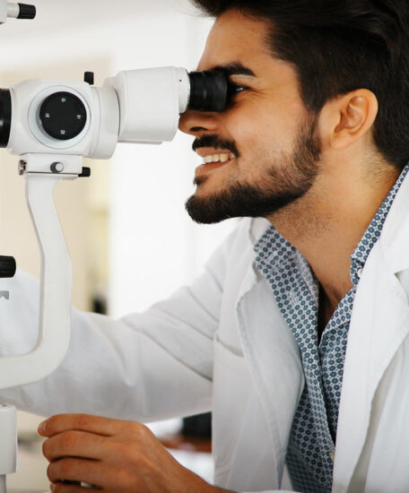 A man in a lab coat examining samples under a microscope for eye diseases.